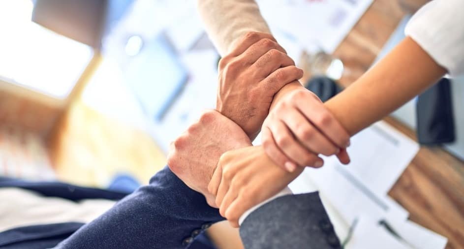 4 co-workers clasping wrists in unity